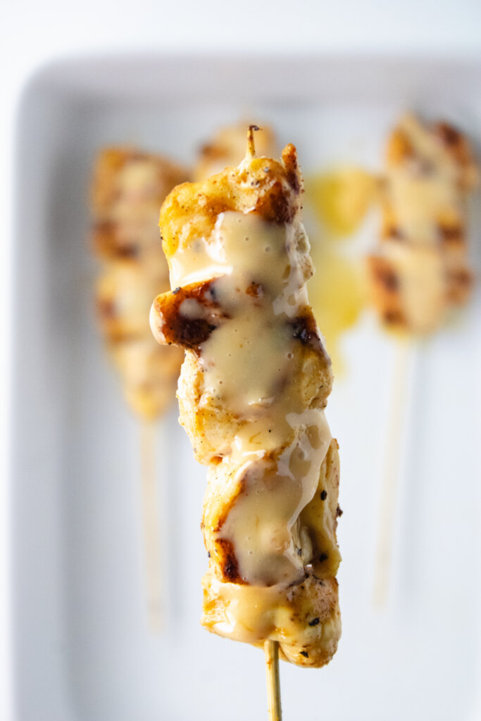 bang bang chicken skewer hovers above white dish
