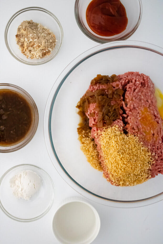 ground beef with seasonings in a clear glass bowl, surrounded by the gravy ingredients for salisbury steak